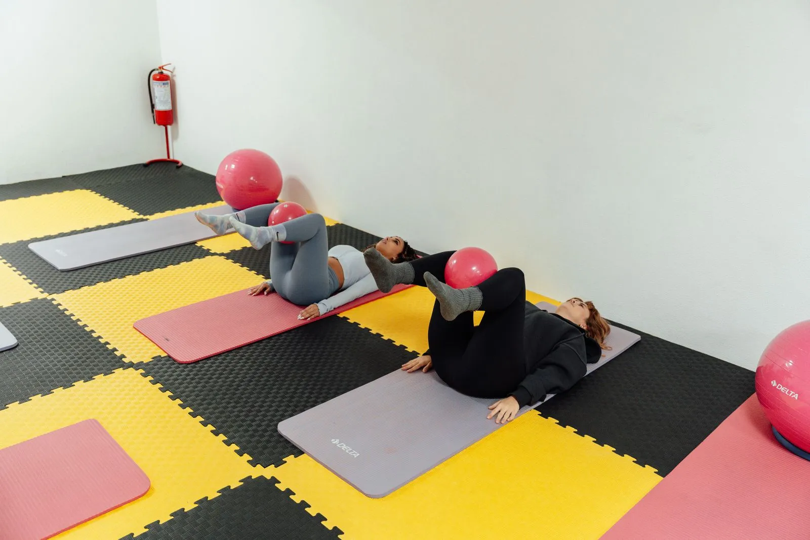 Women in a yoga class using exercise balls on colorful mats indoors.